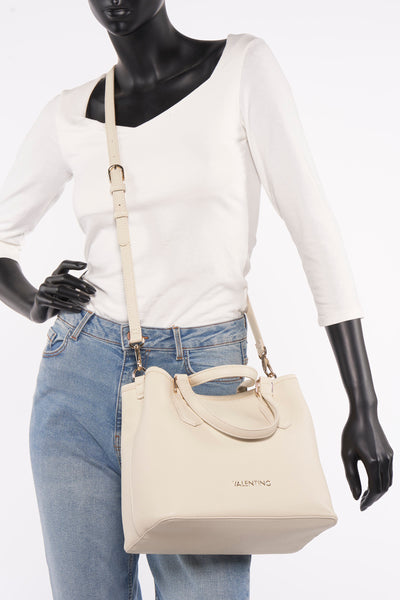 Ecru handtas van VALENTINO BAGS, gedragen over de schouder door een model, met een verstelbare schouderriem en gouden afwerkingen.