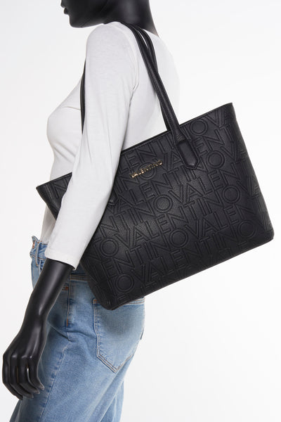 Zwarte handtas van VALENTINO BAGS met reliëf logo patroon, gedragen door een model in spijkerbroek en witte top.