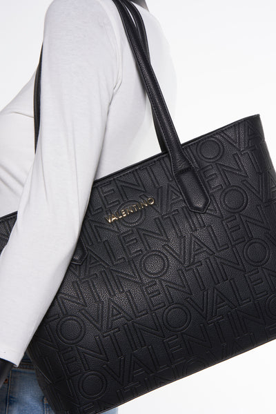Zwarte handtas van VALENTINO BAGS met reliëfletterpatroon en schouderriem, gedragen met een witte trui.