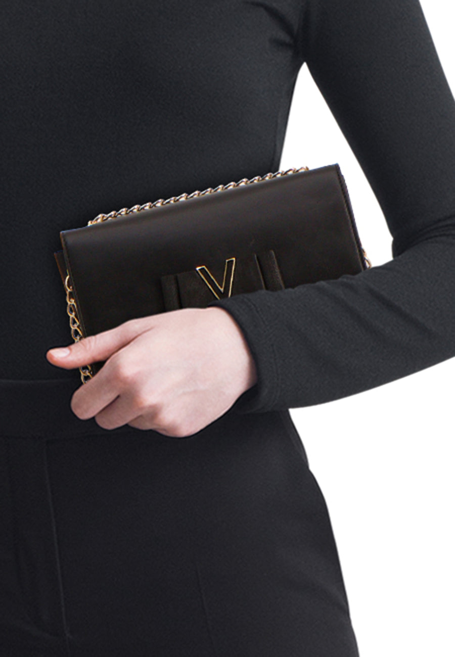 Zwarte VALENTINO BAGS schoudertas met gouden ketting, gedragen met een zwarte outfit.