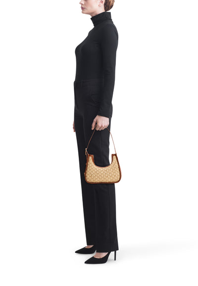 Cognac leather-trimmed woven crossbody bag with structured shape, worn by model in side view with black turtleneck and trousers