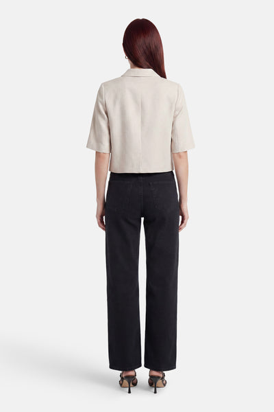 Beige blazer van CAROLL, van achteren gezien, met korte mouwen, gedragen met een zwarte jeans en hoge hakken.