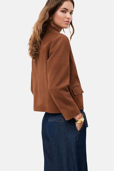Veste courte brun de CAROLL en aspect daim, avec col et une poche à rabat, portée sur un jean foncé avec un bracelet doré.
