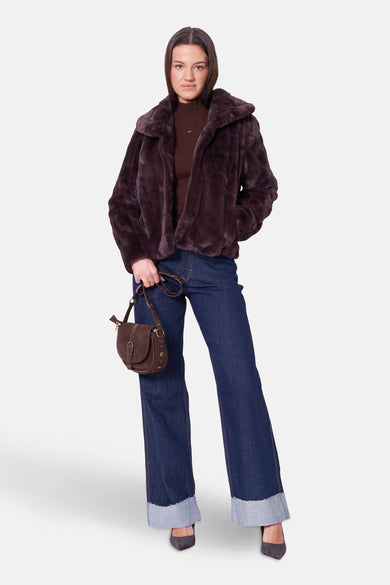 Kort bruin fauxbont jasje van Guess, gedragen met een bruine trui, een spijkerbroek en een handtas.