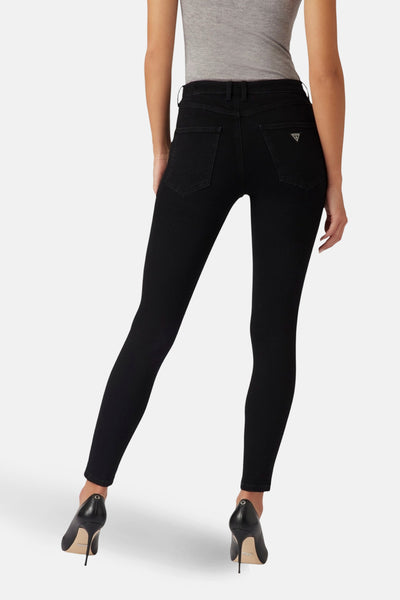 Jean skinny noir de Guess, avec poches arrière et logo triangulaire, porté avec un haut gris et des talons aiguilles noirs.
