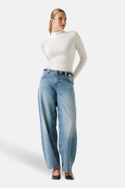 Ecru T-shirt met lange mouwen van Guess, gedragen met een wijde blauwe jeans en bruine schoenen met krokodillenprint.