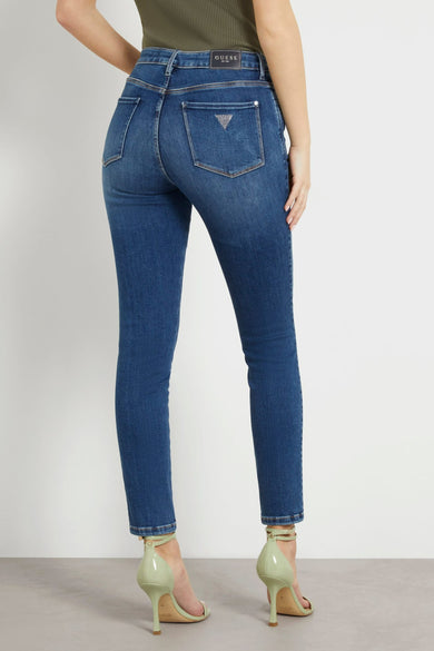 Jean skinny bleu de Guess, avec logo sur poche arrière et chaussures à talons vert clair.