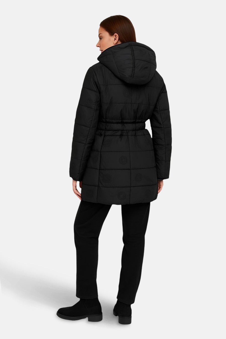 Zwarte lange jas van Guess, met capuchon en riem, gedragen met een zwarte broek en enkellaarsjes.