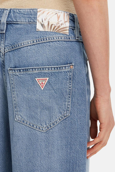 Jean large en denim bleu moyen de Guess, avec patch logo sur la poche arrière et étiquette à la taille.
