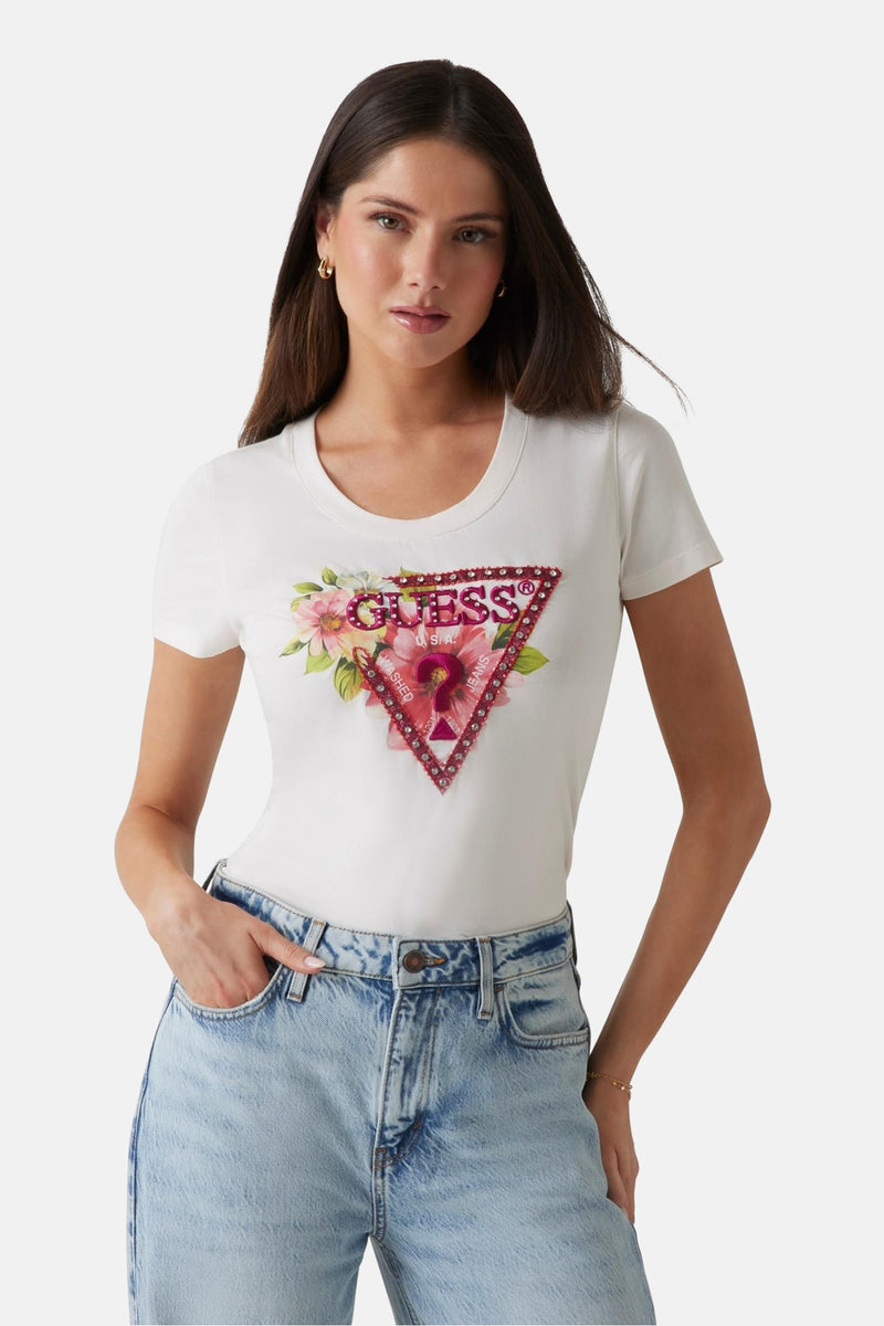 Wit T-shirt met korte mouwen van Guess, versierd met een bloemenlogo en strassteendecoraties, gedragen met een lichte spijkerbroek.
