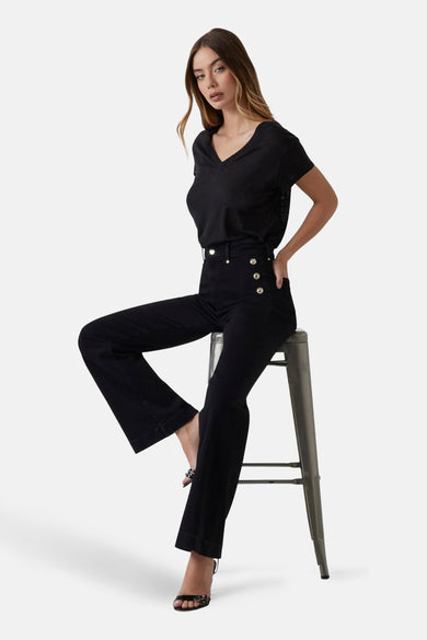 Jean évasé en denim noir de Guess®, porté avec un t-shirt noir et des sandales à talons.