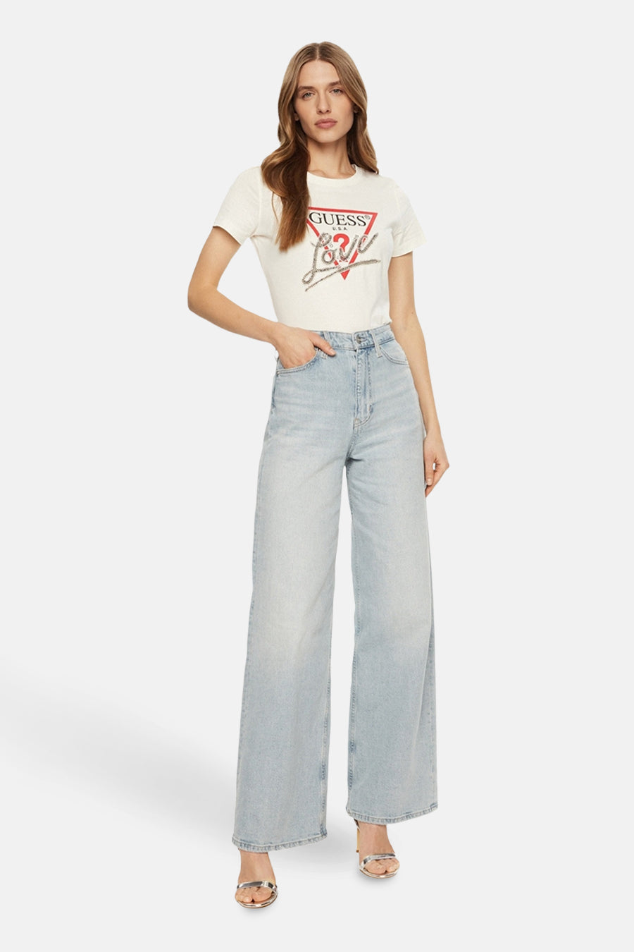 Witte T-shirt met korte mouwen van Guess, versierd met een glinsterend logo en opschrift, gedragen met een wijde high-waisted jeans.