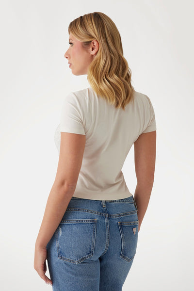 T-shirt écru à manches courtes de Guess, porté avec un jean bleu taille haute.