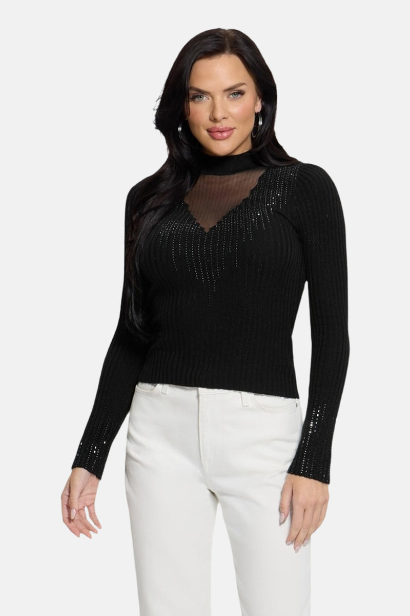 Pull col montant noir de Guess orné de strass, porté avec un pantalon blanc.
