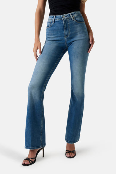 Uitlopende jeans in middinblauw denim van Guess, gedragen met een zwarte top en hoge hakken.