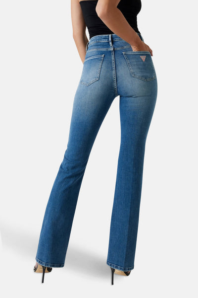 Jean évasé en denim bleu moyen de Guess, porté avec un haut noir et des talons hauts.