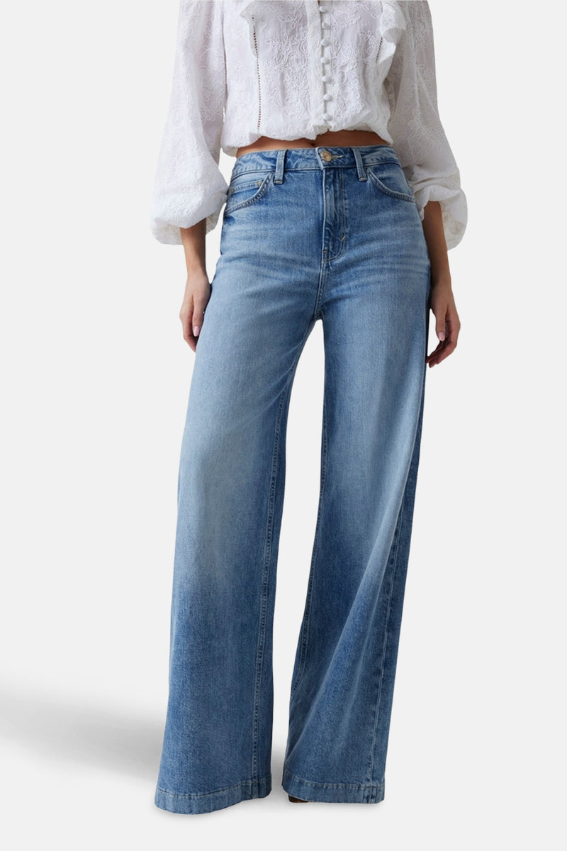 Wijde spijkerbroek in middinblauw denim van Guess, gedragen met een geborduurd wit bloesje.