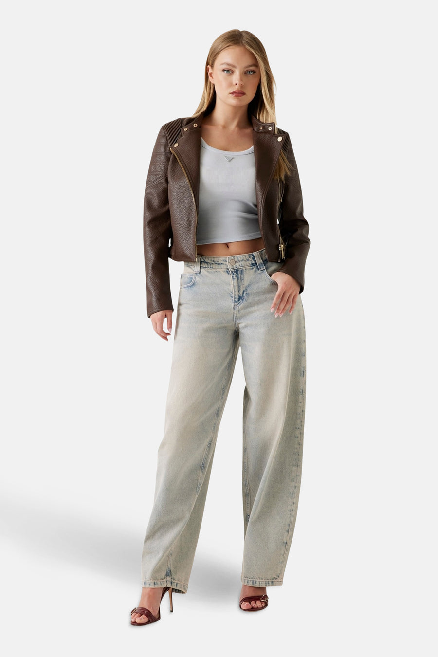 Veste en similicuir marron de Guess, avec une fermeture éclair dorée, portée avec un haut et un jean larges.