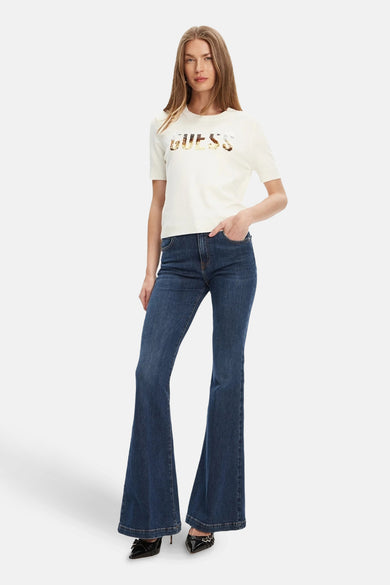 Pull écru à col rond de Guess, orné du logo de la marque, porté avec un jean évasé.