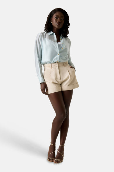Short beige taille haute plissé de Guess®, avec revers, porté par un mannequin avec chemise et sandales.
