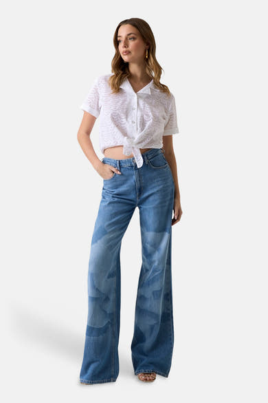 Wit blouseje met korte mouwen van Guess® in ajourbroderie met een knoopsluiting aan de voorkant, gedragen met een wijde jeans.