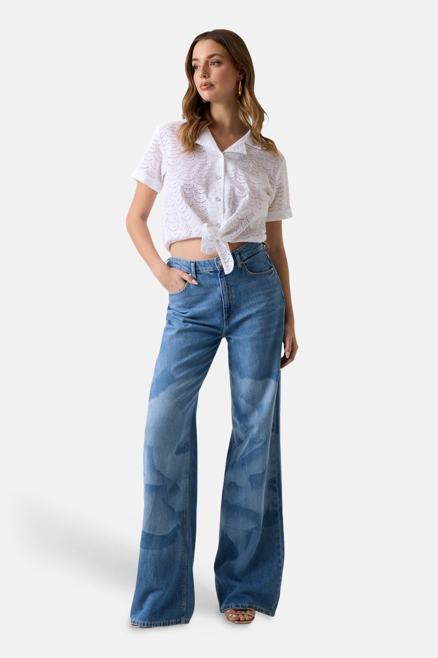 Wit blouseje met korte mouwen van Guess® in ajourbroderie met een knoopsluiting aan de voorkant, gedragen met een wijde jeans.