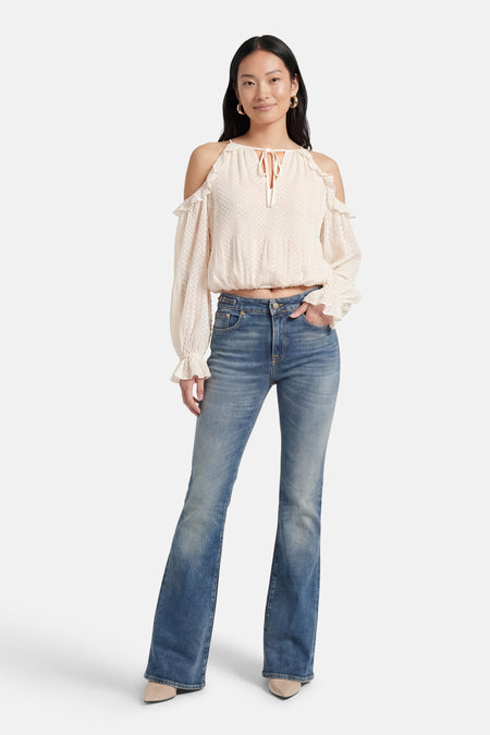 Chemisier écru à manches longues de Guess, avec épaules dénudées, volant décoratif et porté avec un jean.