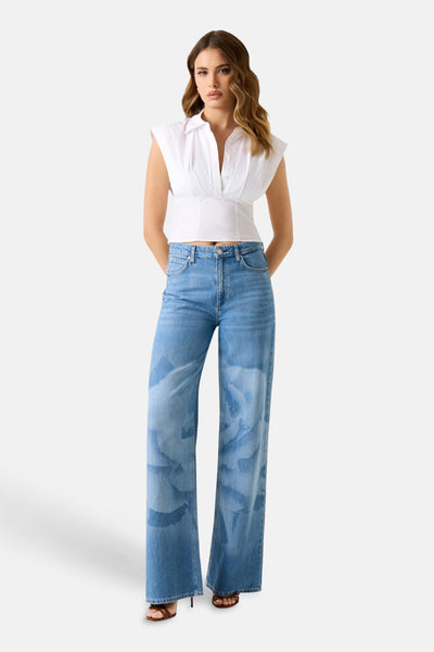Chemisier blanc sans manches de Guess® avec col, décolleté en V et coupe courte, porté avec un jean large.