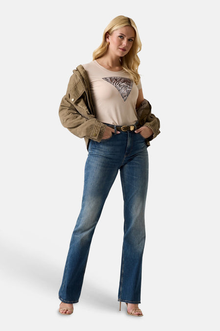 T-shirt à manches courtes beige de Guess avec un motif triangulaire zébré et feuilles de palmier, porté avec un jean et une veste kaki.