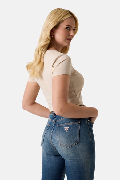 T-shirt court à manches courtes beige de Guess, coupe ajustée, porté avec un jean bleu taille haute.