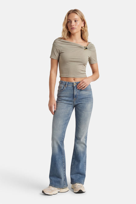 T-shirt vert de Guess, avec un détail plissé à l'épaule, porté avec un jean évasé et des baskets.