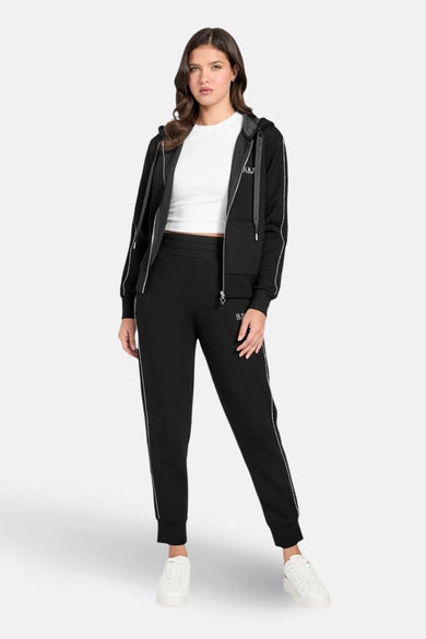 Survêtement noir de Guess, composé d'un sweat zippé à capuche et d'un pantalon de jogging, avec des détails de rayures blanches.