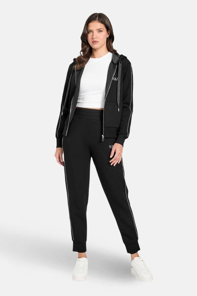 Survêtement noir de Guess, composé d'un sweat zippé à capuche et d'un pantalon de jogging, avec des détails de rayures blanches.
