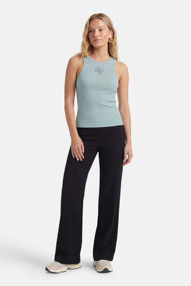 Top sans manches vert de Guess, avec un logo décoratif et une texture côtelée, porté avec un pantalon noir et des chaussures de sport.
