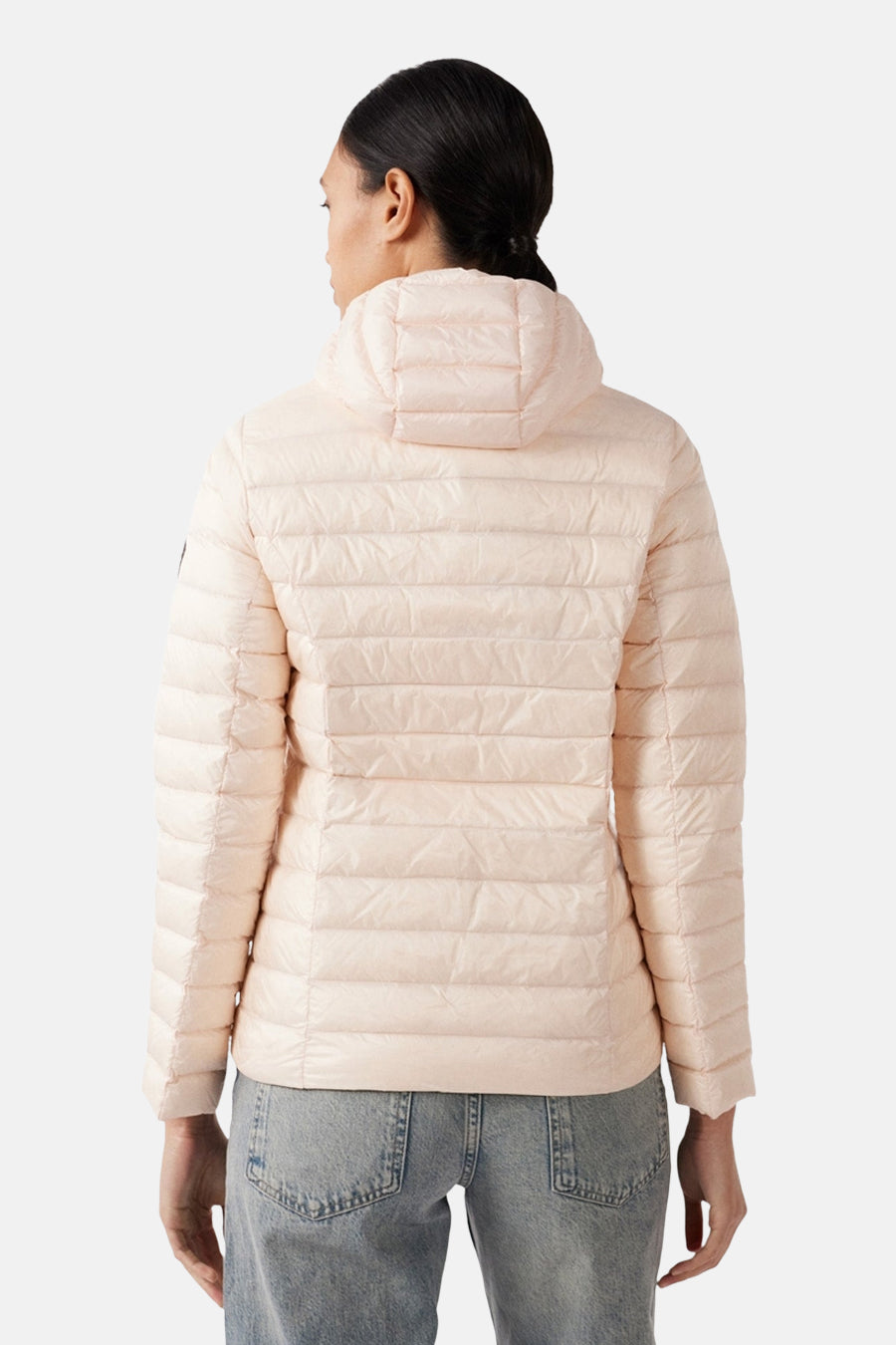 Veste de pluie rose par JOTT, avec capuche et motif matelassé, portée avec un jean.
