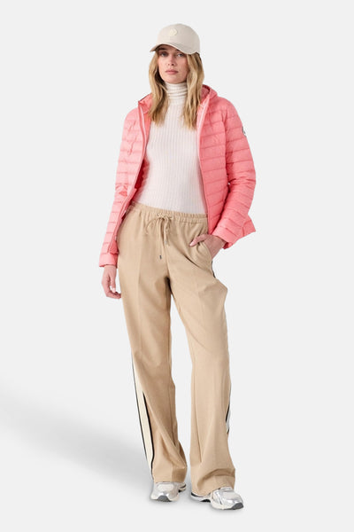 Veste de pluie rose par JOTT, portée avec un pantalon beige à rayures et un col roulé crème.