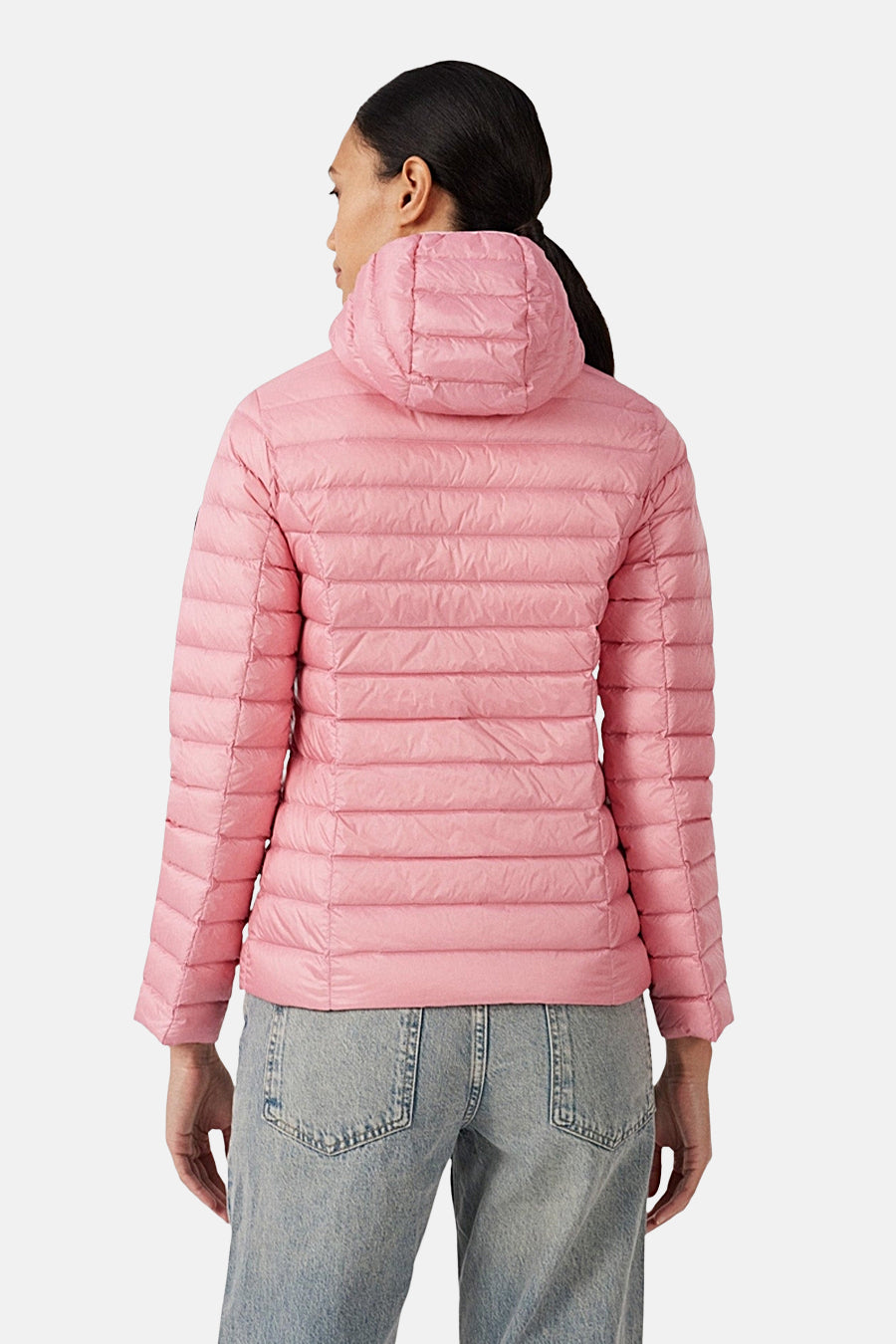 Veste de pluie rose par JOTT, avec capuche, portée avec un jean bleu, vue de dos.