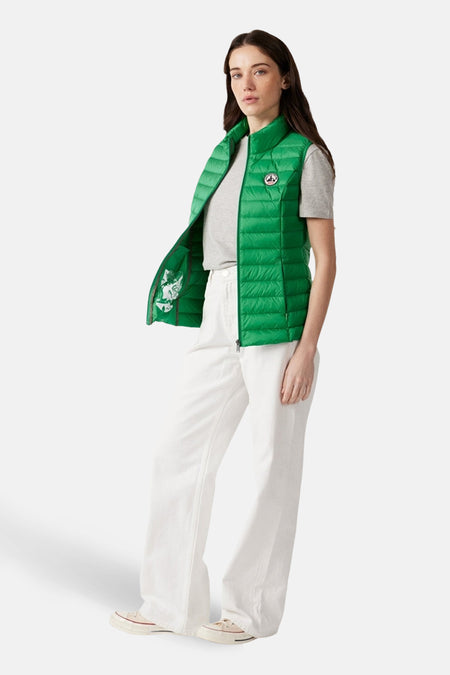 Veste sans manches vert de JOTT, portée avec un t-shirt gris et un pantalon blanc ample.