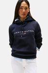 Donkerblauwe hoodie van TOMMY HILFIGER, met wit logo op de voorkant, gedragen over een lichtblauw overhemd en een witte broek.