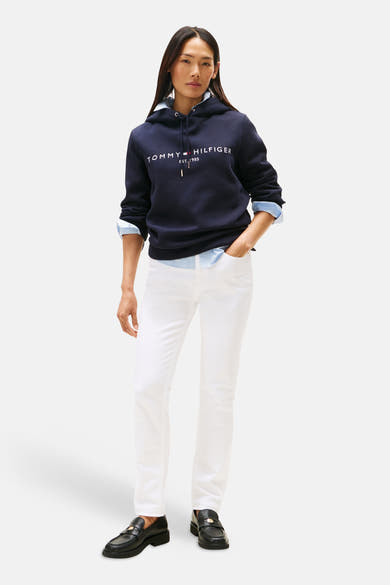 Sweat à capuche bleu marine de TOMMY HILFIGER, avec logo blanc sur le devant, porté sur une chemise bleu clair et un pantalon blanc.