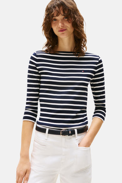 Blauw-wit gestreept T-shirt van Tommy Jeans, gedragen met een witte broek en een zwarte riem.
