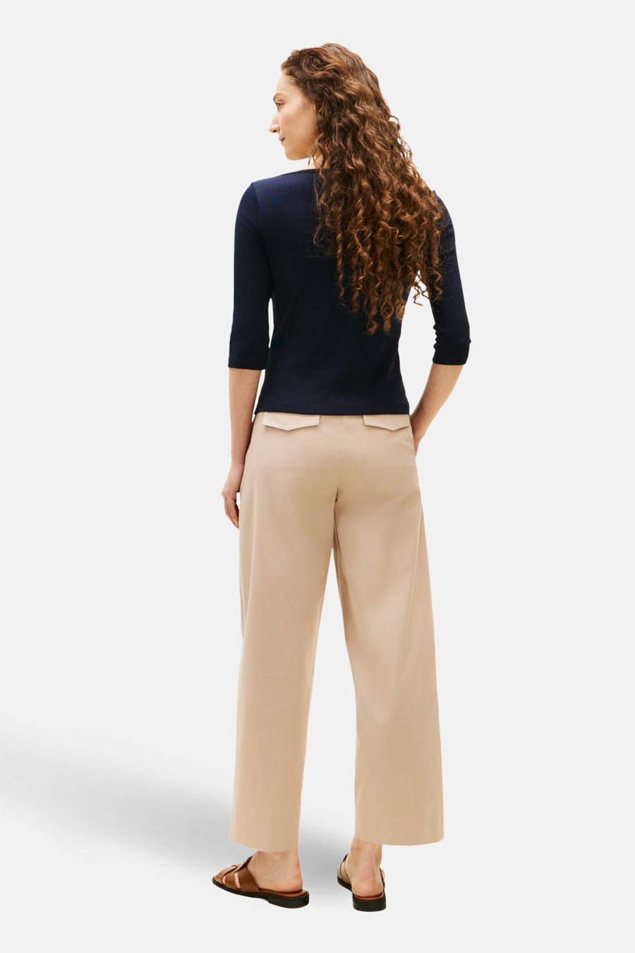 Donkerblauwe T-shirt met 3/4 mouwen van TOMMY JEANS, gedragen met een beige broek met hoge taille en bruine leren sandalen.