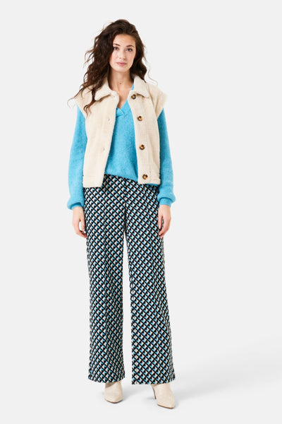 Veste sans manches écru de GARCIA avec col en fausse fourrure, portée sur un pull bleu et un pantalon à motifs.
