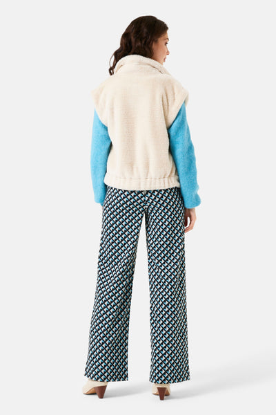 Veste sans manches écru de Garcia, avec un pull bleu clair et un pantalon à motifs géométriques.