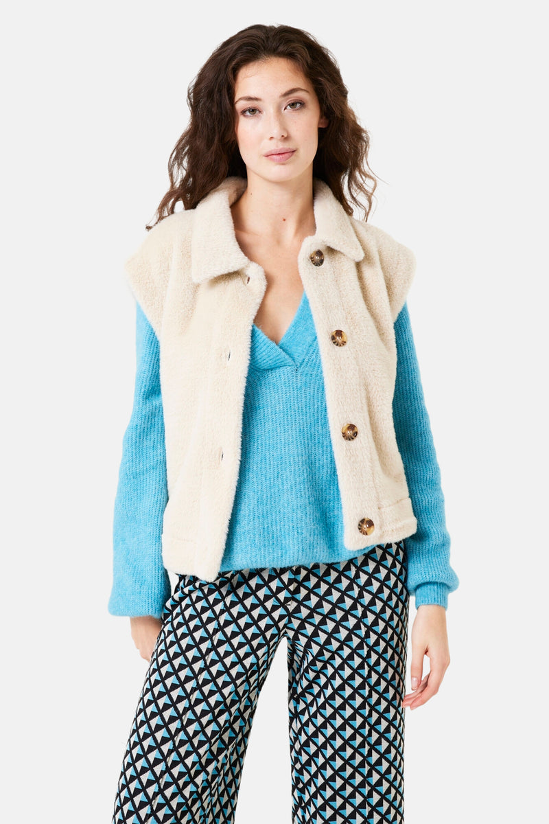 Veste écru sans manches de GARCIA avec boutons marron, portée sur un pull bleu clair et un pantalon à motifs.
