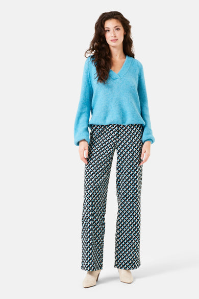 Pantalon noir à motifs graphiques par GARCIA, porté avec un pull bleu en maille et des bottines couleur crème.
