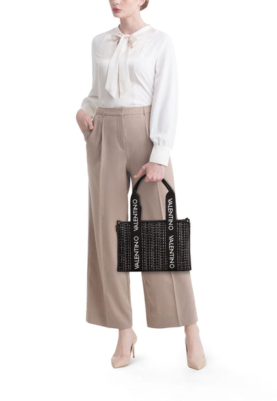 Sac à main noir par Valentino Bags avec un motif quadrillé et des anses griffées, porté avec un chemisier ivoire.
