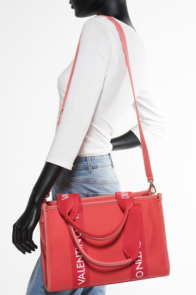 Sac à main orange de VALENTINO BAGS porté à l'épaule par un mannequin, avec bandoulière et jean bleu clair.

