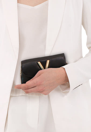 Zwarte schoudertas van VALENTINO BAGS, in de hand gedragen met een witte jas en een witte top.