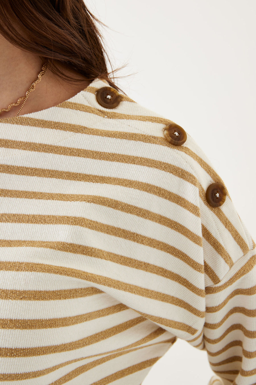 Ecru sweatshirt with gold stripes by GARCIA, decorated with decorative brown buttons on the shoulder, worn with a gold necklace.